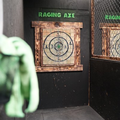 Axe throwing target board with numbers inside a fenced enclosure.