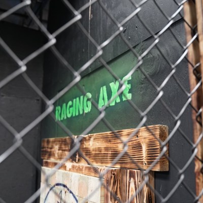 Sign reads 'Raging Axe' behind a chain-link fence with wood paneling visible.