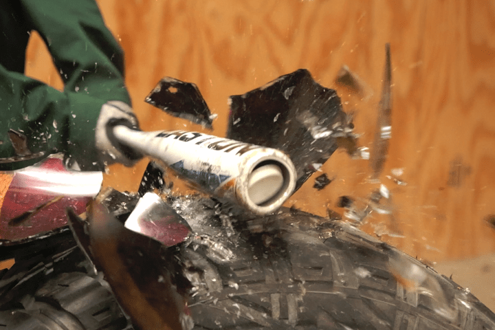 Person in green jacket smashing a TV with a metal bat, with glass shattering.