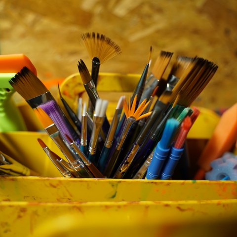 Assorted paintbrushes and sponges in a colorful holder.