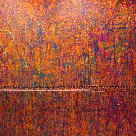 Abstract graffiti wall with orange and purple colors, metal grate, and trash can.