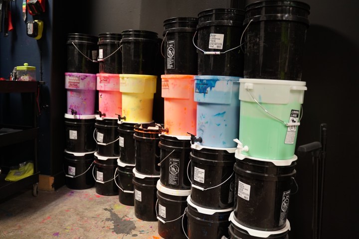 Stacked black and colorful paint buckets against a dark wall in a studio.