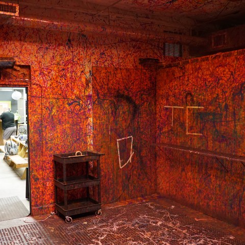 Colorfully splattered room with open door to another space and a cart on the floor.
