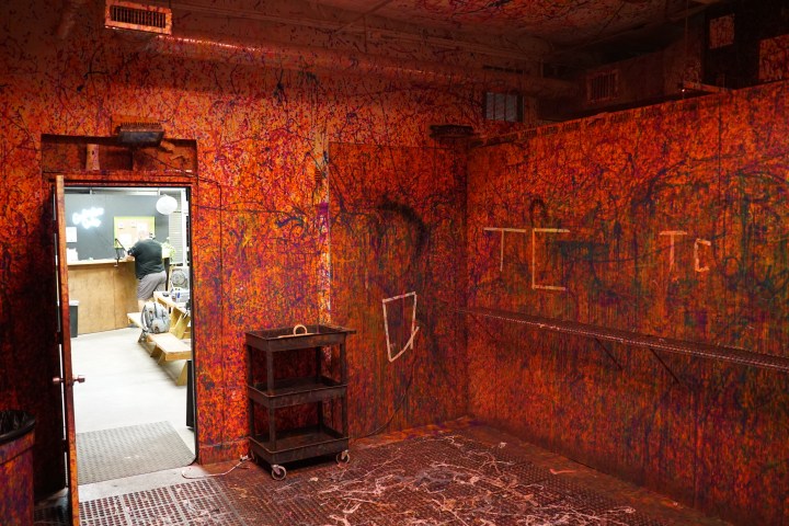 Colorfully splattered room with open door to another space and a cart on the floor.