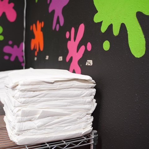 Stack of white towels on a shelf with colorful splatter wall art background.