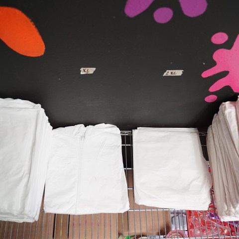 Folded white shirts stacked by size on a shelf, wall with colorful paint splatters in the background.