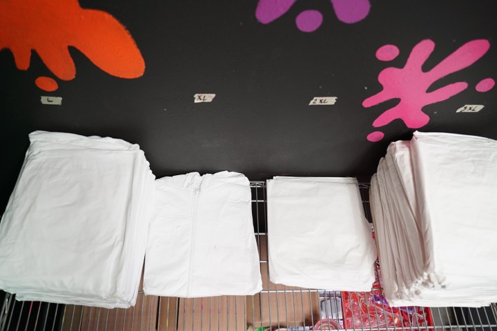 Folded white shirts stacked by size on a shelf, wall with colorful paint splatters in the background.