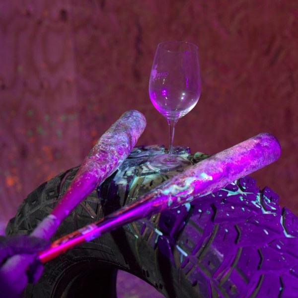 Wine glass on tire with two paint-splattered bats, purple lighting.