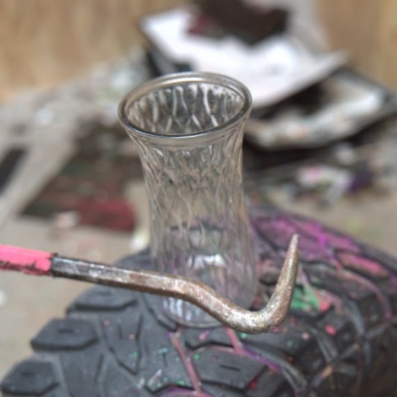 Glass vase on tire with painted crowbar resting on it.